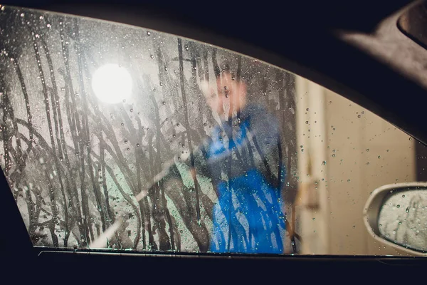 Человек стирает автомобиль ручной мойки автомойки самообслуживания, уборка с пеной, под давлением воды. Стиральная машина в станции самообслуживания с высоким давлением бластер окно просматривается изнутри автомобиля — стоковое фото