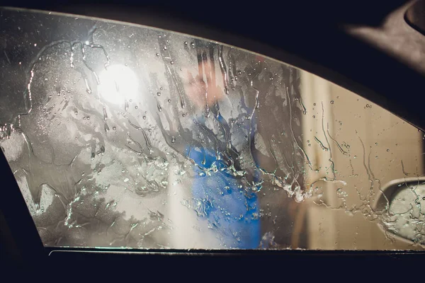 man washing automobile manual car washing self service,cleaning with foam,pressured water. Washing car in self service station with high pressure blaster window viewed from inside car