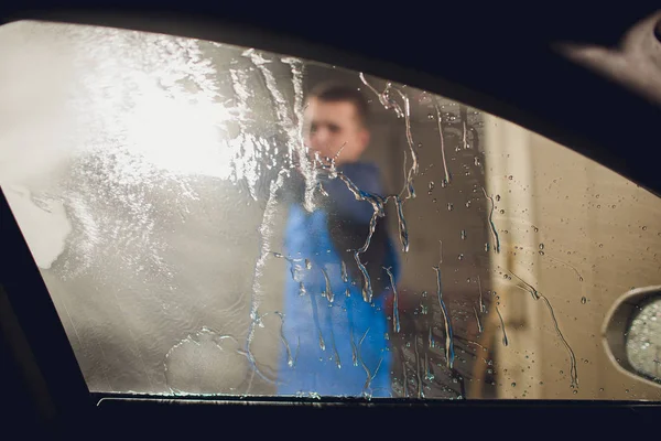 Man washing automobile manual car washing self service,cleaning with foam,pressured water. Washing car in self service station with high pressure blaster window viewed from inside car — Stock Photo, Image