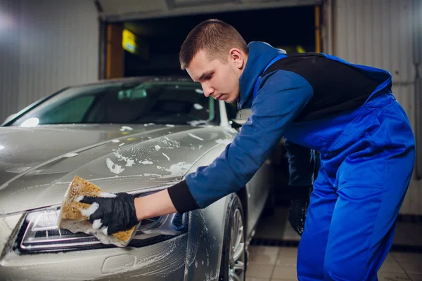 Открытая автомойка с желтой губкой. Красивый мужчина моет машину — стоковое фото