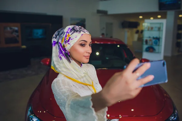 Property and people concept - muslim woman in hijab with car key over car show background. happy woman taking car key from dealer in auto show or salon — Stockfoto