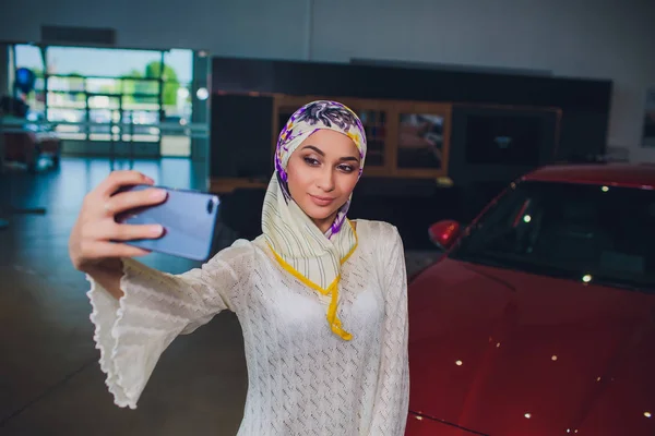 Propiedad y el concepto de la gente - mujer musulmana en hijab con la llave del coche sobre el fondo del espectáculo de coches. mujer feliz tomando la llave del coche del distribuidor en el espectáculo auto o salón — Foto de Stock