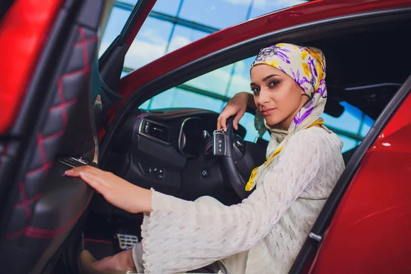 Property and people concept - muslim woman in hijab with car key over car show background. happy woman taking car key from dealer in auto show or salon — Stockfoto