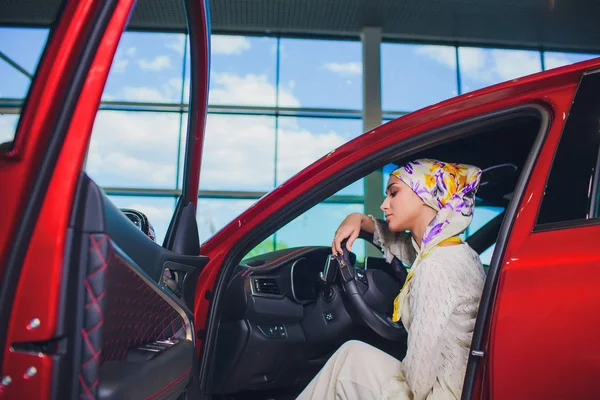 Propiedad y el concepto de la gente - mujer musulmana en hijab con la llave del coche sobre el fondo del espectáculo de coches. mujer feliz tomando la llave del coche del distribuidor en el espectáculo auto o salón — Foto de Stock