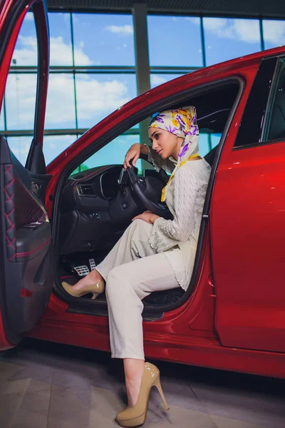 Propiedad y el concepto de la gente - mujer musulmana en hijab con la llave del coche sobre el fondo del espectáculo de coches. mujer feliz tomando la llave del coche del distribuidor en el espectáculo auto o salón —  Fotos de Stock