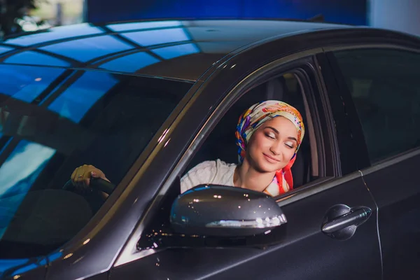 Propiedad y el concepto de la gente - mujer musulmana en hijab con la llave del coche sobre el fondo del espectáculo de coches. mujer feliz tomando la llave del coche del distribuidor en el espectáculo auto o salón — Foto de Stock