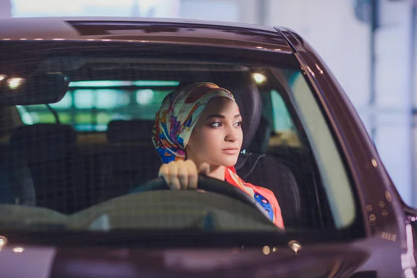 Propiedad y el concepto de la gente - mujer musulmana en hijab con la llave del coche sobre el fondo del espectáculo de coches. mujer feliz tomando la llave del coche del distribuidor en el espectáculo auto o salón — Foto de Stock