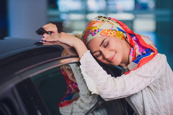 Propiedad y el concepto de la gente - mujer musulmana en hijab con la llave del coche sobre el fondo del espectáculo de coches. mujer feliz tomando la llave del coche del distribuidor en el espectáculo auto o salón — Foto de Stock