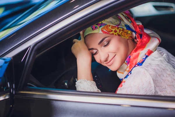 Propiedad y el concepto de la gente - mujer musulmana en hijab con la llave del coche sobre el fondo del espectáculo de coches. mujer feliz tomando la llave del coche del distribuidor en el espectáculo auto o salón —  Fotos de Stock