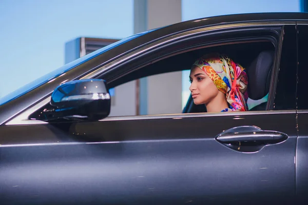 Propiedad y el concepto de la gente - mujer musulmana en hijab con la llave del coche sobre el fondo del espectáculo de coches. mujer feliz tomando la llave del coche del distribuidor en el espectáculo auto o salón —  Fotos de Stock