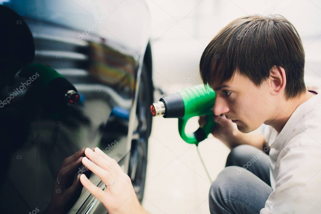 Master installs tint film for car with hairdryer. Concept protection car