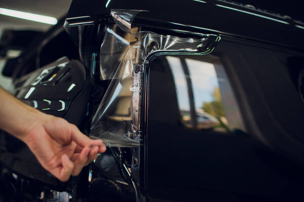 Worker hands installs car paint protection film wrap.