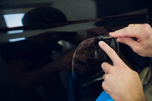 Worker hands installs car paint protection film wrap.
