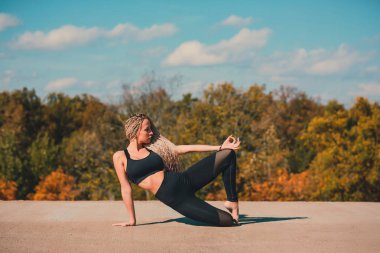 Büyük şehirde bir gökdelenin çatı üzerinde yoga yaparken kadın.