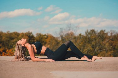Büyük şehirde bir gökdelenin çatı üzerinde yoga yaparken kadın.