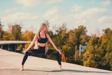 Büyük şehirde bir gökdelenin çatı üzerinde yoga yaparken kadın.