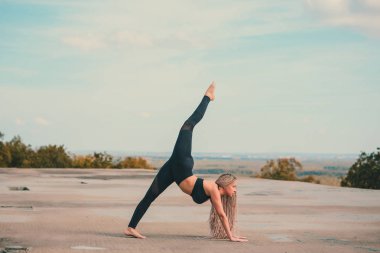 Büyük şehirde bir gökdelenin çatı üzerinde yoga yaparken kadın.