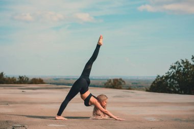 Büyük şehirde bir gökdelenin çatı üzerinde yoga yaparken kadın.