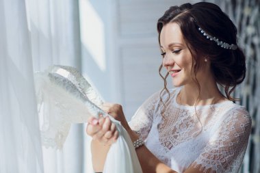 İpek sabahlık ve dantelli peçe gelinlik pencerenin yakınındaki bir askı tutan çok esmer gelin.