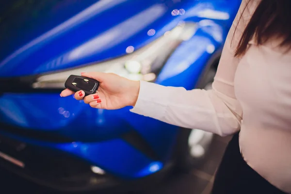 Mujer sosteniendo las llaves del coche con el coche en el fondo —  Fotos de Stock