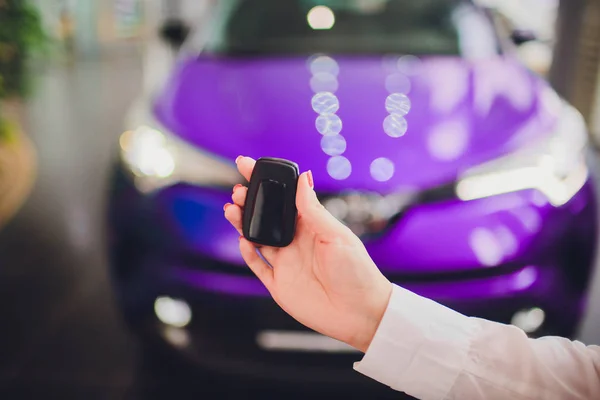 Hembra sosteniendo las llaves del coche con el coche en color púrpura de fondo —  Fotos de Stock