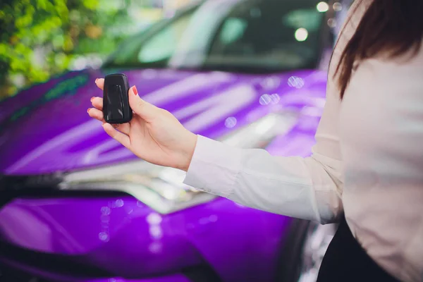 Hembra sosteniendo las llaves del coche con el coche en color púrpura de fondo —  Fotos de Stock
