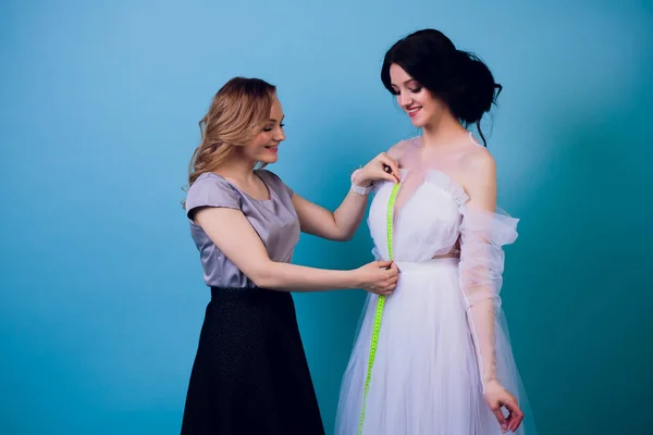 Hermosa costurera mujer con el pelo largo y el cliente. sastre crea imagen para el cliente en taller de costura. dressmaker mide chica con cinta métrica. Concepto de diseño de moda —  Fotos de Stock