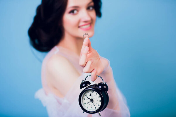 Beautiful charming girl in white wedding dress, being late in morning, and holding in her hand retro alarm clock and ring