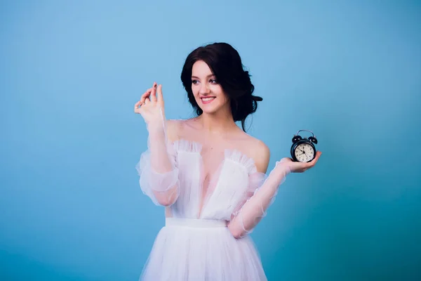 Menina encantadora bonita em vestido de noiva branco, sendo tarde de manhã, e segurando em sua mão despertador retro e anel — Fotografia de Stock