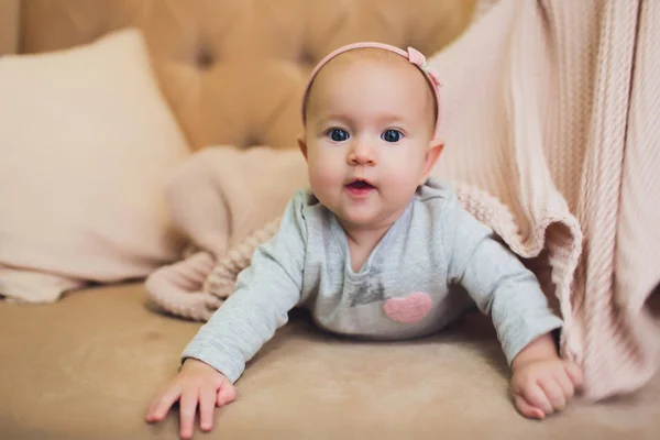 Dziewczyna Słodkie noworodek leżąc na kanapie, patrząc w kierunku kamery. 6-7 miesięcy życia niemowlę na brzuch podnoszenia górnej części ciała. — Zdjęcie stockowe
