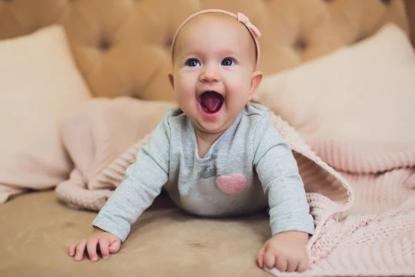 Sweet adorable baby girl lying on a couch looking towards camera. 6-7 months old infant on belly lifting upper body. — Stock Photo, Image