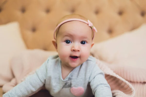 Sweet adorable baby girl lying on a couch looking towards camera. 6-7 months old infant on belly lifting upper body. — Stock Photo, Image