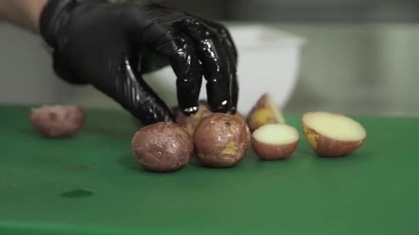 La mano de un hombre se pela con un cuchillo rojo una papa sobre una mesa de granito negro con muchas otras patatas en el fondo. Preparación de patatas a cocer . — Vídeo de stock