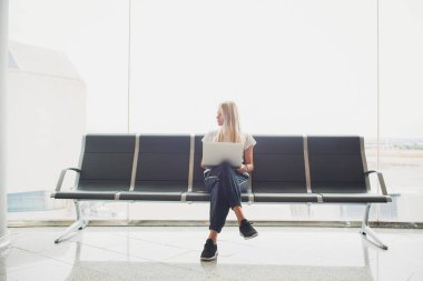 Onun uçuş havaalanı terminalinde bekliyor, sandalyede oturan ve yan seyir dizüstü bilgisayarda yazarak kadın. Üstten görünüm.