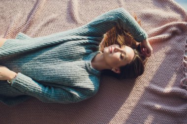Yatak odasında poz, rahat gri kazak ve örme çorap giyen güzel seksi tan esmer kadın. Dinlen, uyku, konfor kavramı. Genç kadının evde yatakta yatan kapatın. İskandinav ev.