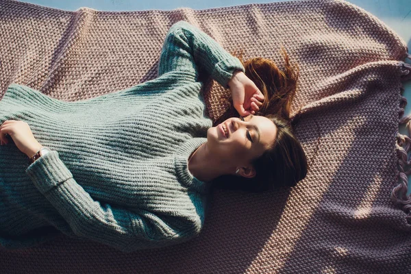 Belle femme brune bronzée sexy posant dans la chambre, portant un pull gris confortable et des chaussettes tricotées. Repos, sommeil, concept de confort. Gros plan d'une jeune femme couchée dans son lit à la maison. Maison scandinave . — Photo