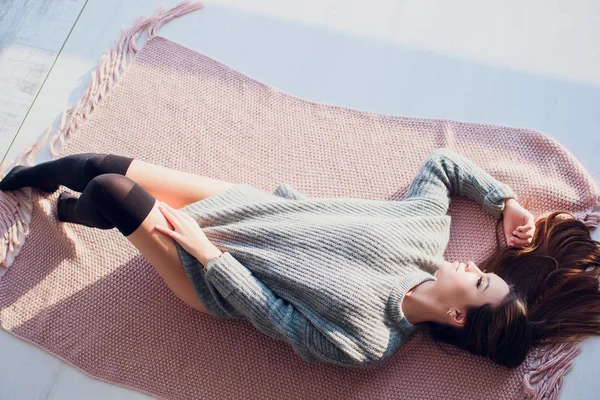 Beautiful sexy tan brunette woman posing in bedroom, wearing cozy grey sweater and knitted socks. Rest, sleeping, comfort concept. Close up of young woman lying in bed at home. Scandinavian home. — Stock Photo, Image