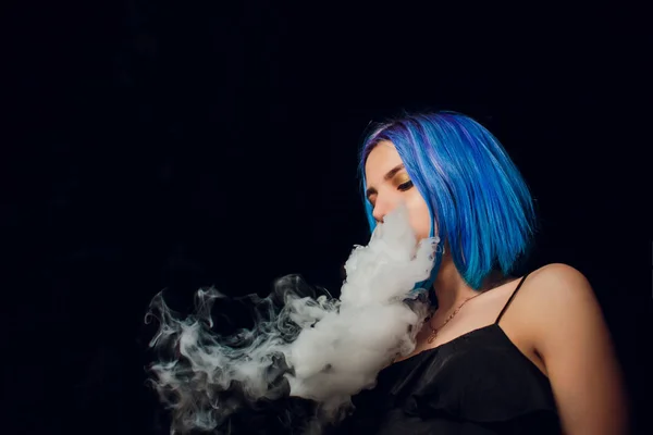 Young woman smoking electronic cigarette against a black background — Stock Photo, Image