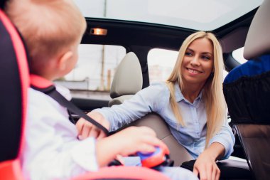 Aile, taşıma, yol çelme takmak ve insanlar konsepti - mutlu kadın arabada çocuk emniyet kemeri ile sabitleme