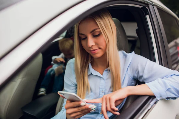 Mujer rubia feliz mostrando teléfono inteligente por la ventana del coche. Centrarse en el teléfono móvil . — Foto de Stock