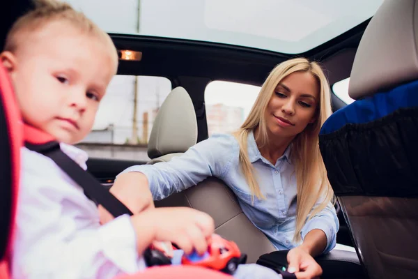 Famille, transport, voyage sur la route et concept de personnes - femme heureuse attachant l'enfant avec la ceinture de sécurité dans la voiture — Photo