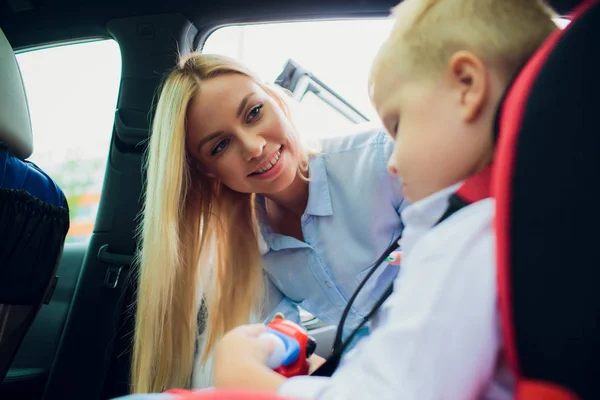 Famille, transport, voyage sur la route et concept de personnes - femme heureuse attachant l'enfant avec la ceinture de sécurité dans la voiture — Photo