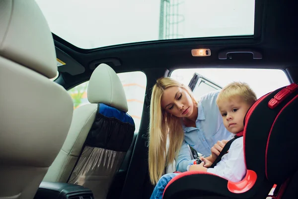 Famille, transport, voyage sur la route et concept de personnes - femme heureuse attachant l'enfant avec la ceinture de sécurité dans la voiture — Photo