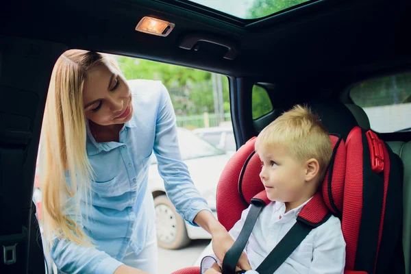 Famille, transport, voyage sur la route et concept de personnes - femme heureuse attachant l'enfant avec la ceinture de sécurité dans la voiture — Photo