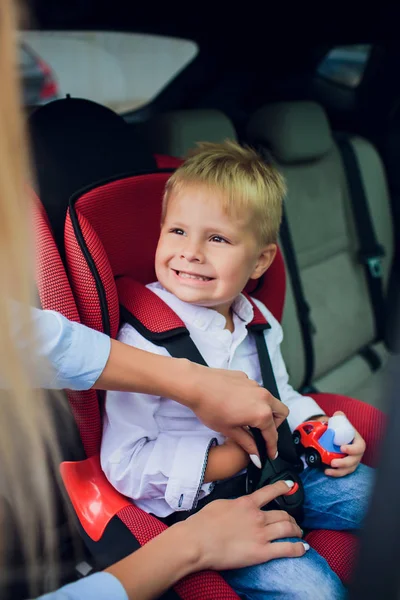 Bébé garçon avec des cheveux bouclés assis dans le siège auto enfant avec voiture jouet dans les mains — Photo