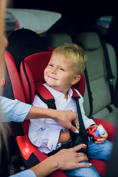 Baby boy with curly hair sitting in child car seat with toy car in hands — Stock Photo, Image