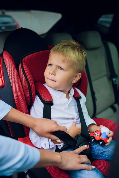 Pojke med lockigt hår sitter i bil barnstol med leksaksbil i händer — Stockfoto