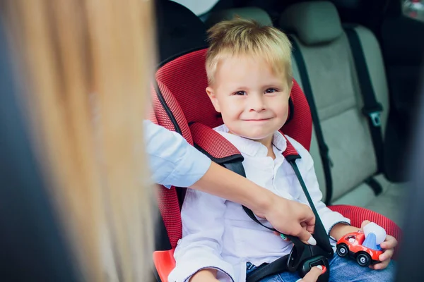 Мальчик с вьющимися волосами сидит в детском автокресле с игрушечной машиной в руках — стоковое фото