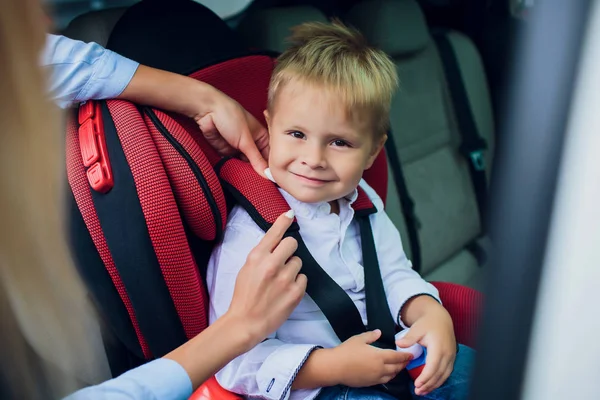 Bébé garçon avec des cheveux bouclés assis dans le siège auto enfant avec voiture jouet dans les mains — Photo