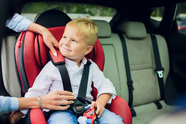 Bébé garçon avec des cheveux bouclés assis dans le siège auto enfant avec voiture jouet dans les mains — Photo